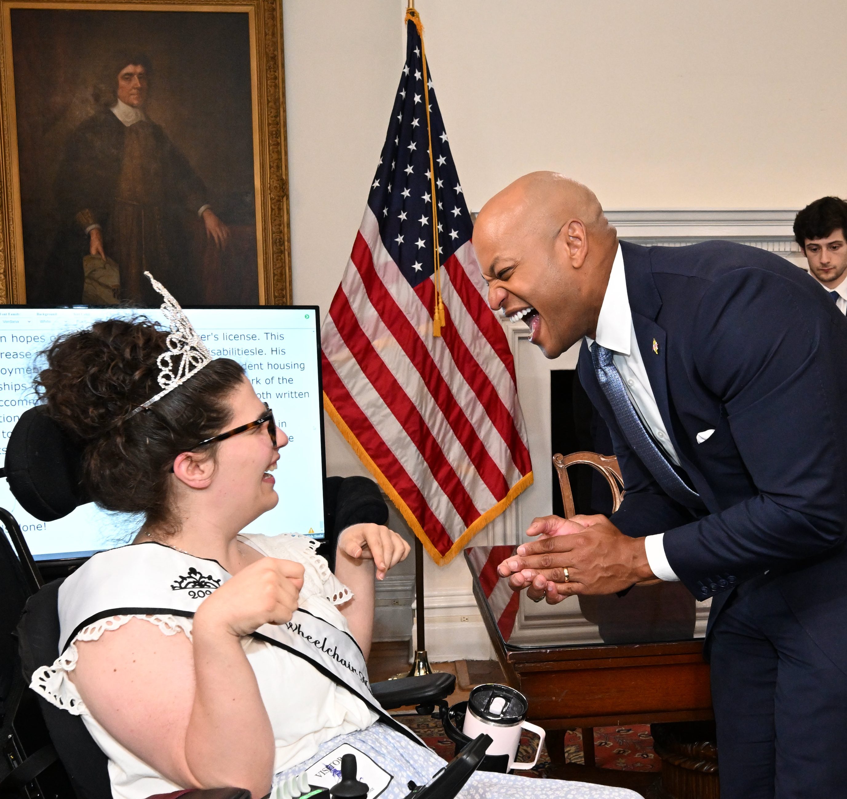 Dominique is laughing with Gov. Wes Moore in her Ms. Wheelchair Maryland sash and tiara. They both have wide smiles.